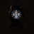 A smartwatch with a round dial is prominently displayed against a dark background. The digital screen shows various information such as time, date, heart rate, and steps. The watch face is illuminated, featuring a design with numbers, while icons indicating activity and heart monitoring are visible.